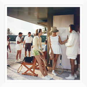 Dressed in vintage tennis attire, a group reminiscent of Slim Aarons gathers outside. Two women lean with rackets against a wall while the others converse, echoing the essence of iconic Soicher Marin's Getty Images product "Tennis in the Bahamas.