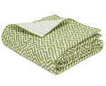 The Gabriel Bedding Collection by Matouk features a green and white geometric-patterned quilt, neatly folded with a flipped corner revealing its white interior accented by blue lines—a refined example of sophisticated geometric motif bedding for any space.