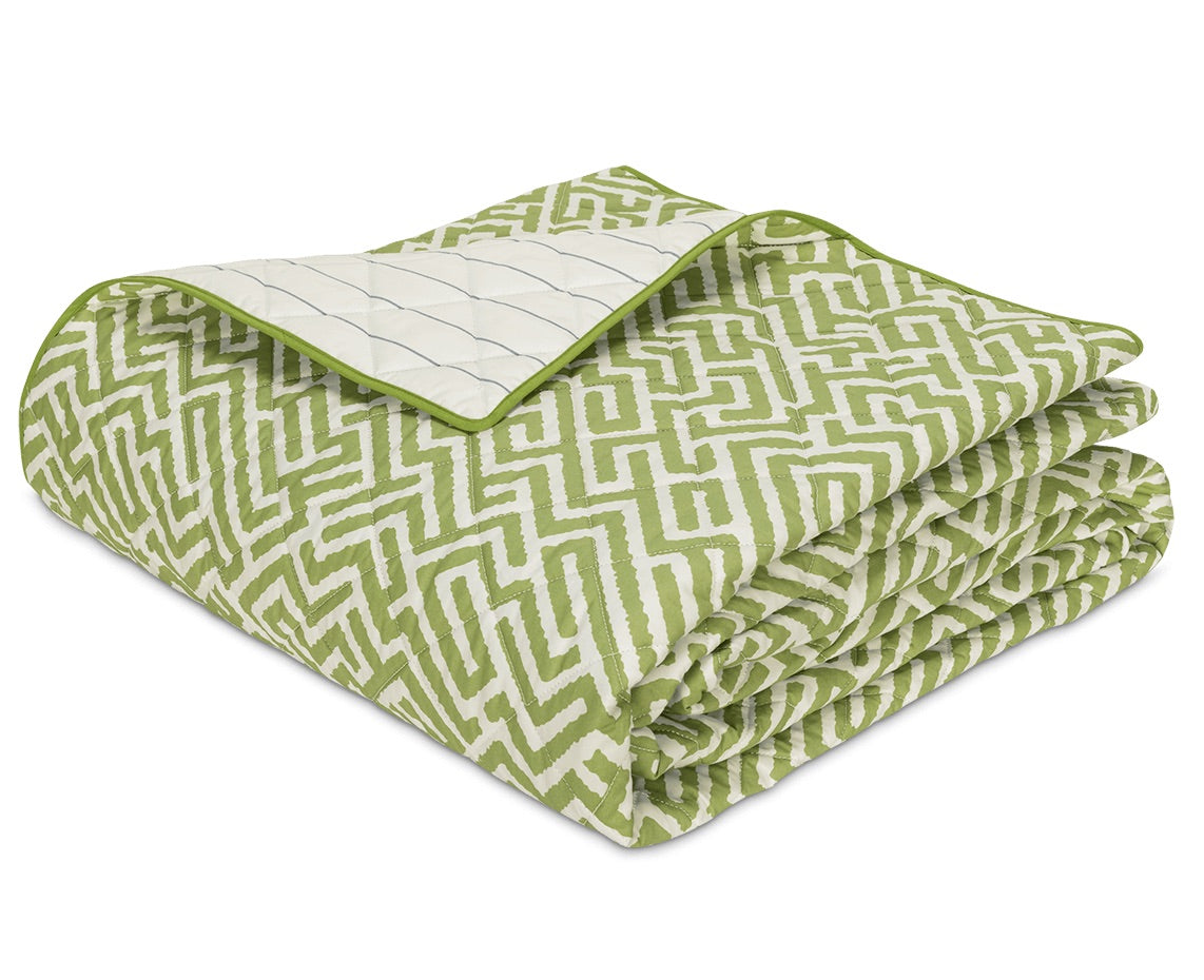 The Gabriel Bedding Collection by Matouk features a green and white geometric-patterned quilt, neatly folded with a flipped corner revealing its white interior accented by blue lines—a refined example of sophisticated geometric motif bedding for any space.
