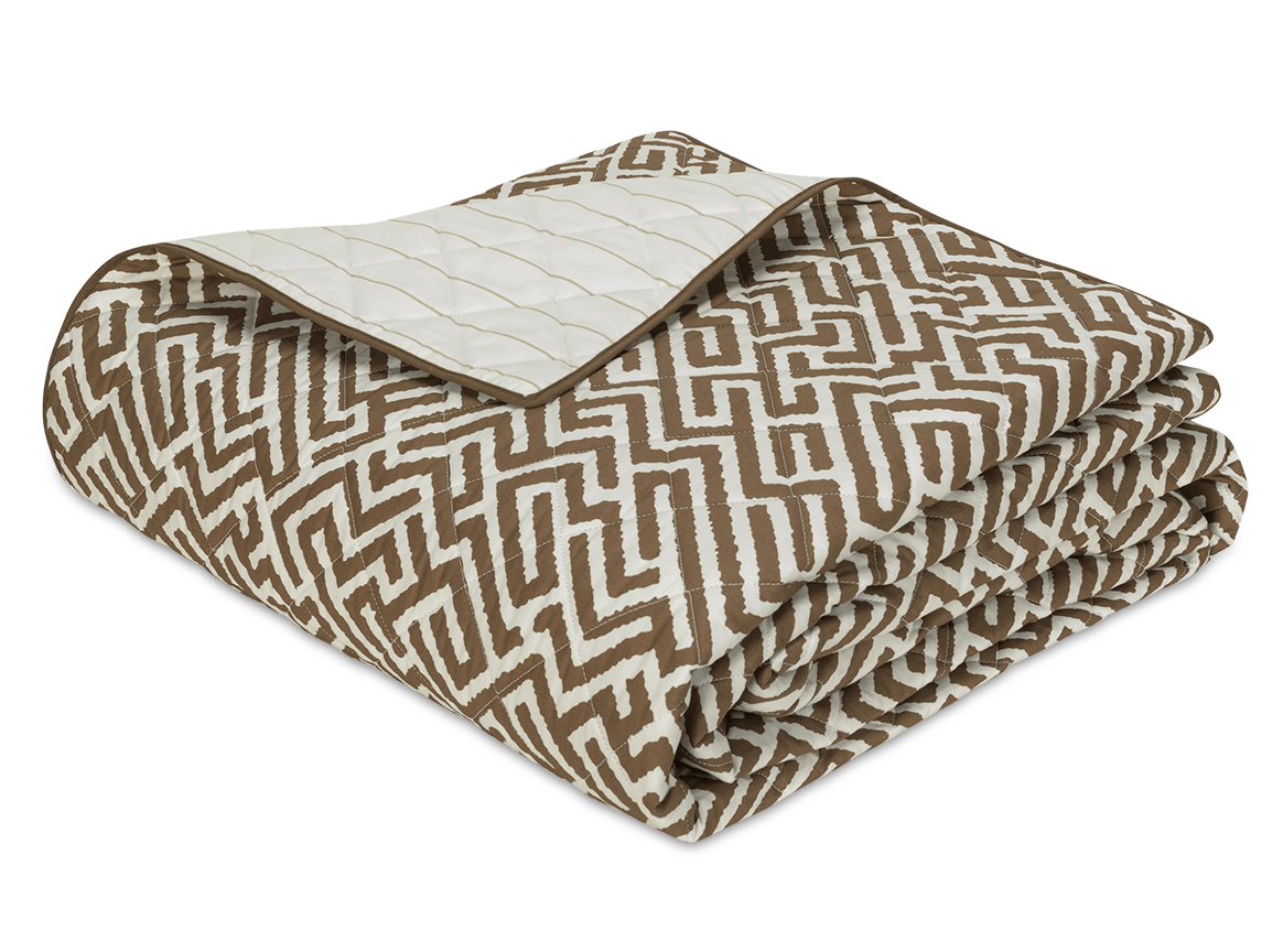 The Gabriel Bedding Collection, Mocha by Matouk features a folded quilt with a brown and white geometric motif on one side and a solid cream quilted design on the other, ideal for layering with Schumacher or woven tapestry bedding.