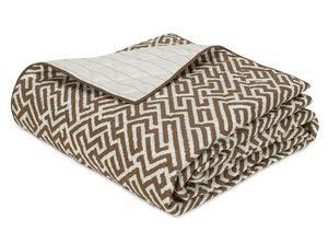 The Gabriel Bedding Collection, Mocha by Matouk features a folded quilt with a brown and white geometric motif on one side and a solid cream quilted design on the other, ideal for layering with Schumacher or woven tapestry bedding.