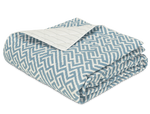 The Gabriel Bedding Collection in Stony Blue by Matouk features a folded quilt with a blue and white geometric motif on top and a plain quilted underside, blending subtle luxury with refined style.