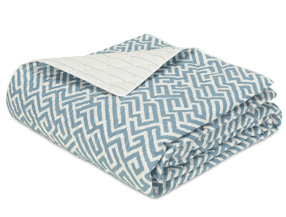 The Gabriel Bedding Collection in Stony Blue by Matouk features a folded quilt with a blue and white geometric motif on top and a plain quilted underside, blending subtle luxury with refined style.