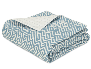 The Gabriel Bedding Collection in Stony Blue by Matouk features a folded quilt with a blue and white geometric motif on top and a plain quilted underside, blending subtle luxury with refined style.