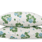 Two white pillowcases from the Matouk Tillett x Matouk Geranium Bedding Collection in blue, featuring a green and blue floral print, are stacked together against a plain background.