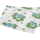The Tillett x Matouk Geranium Bedding Collection in Blue by Matouk showcases folded white percale fabric with a blue and green floral pattern and scalloped edges, displayed against a white background.