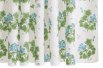 The Matouk Geranium Shower Curtain Collection features a white curtain adorned with green leaves and small blue flowers, inspired by the classic Geranium print and crafted in Luca percale style.