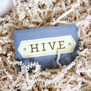 A Hive Gift Card from HIVE Home, Gift and Garden nestles in shredded beige packing paper—an ideal in-store gifting choice.