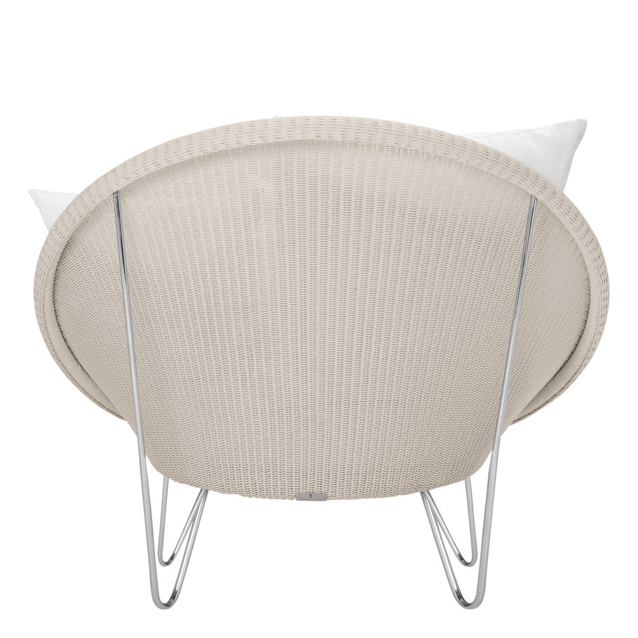 Rear view of Janus et Cie’s Lounge Chair in Schooner Snow: a round, handwoven stainless steel beige chair with a white cushion and metal hairpin legs—ideal for luxury interiors.