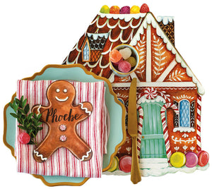 A Gingerbread Partyware Collection placemat shaped like a gingerbread house with a blue plate, red-striped napkin, “Phoebe” gingerbread man place card, gold flatware, and gumdrops.