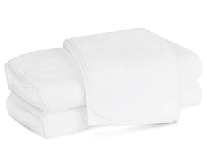 Three neatly folded white towels from the luxurious Matouk Giza Bath Collection, crafted from Egyptian cotton, are stacked on a plain white surface.