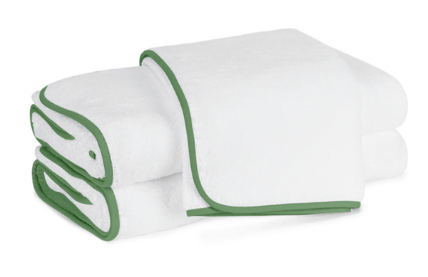 The Matouk Giza Bath Collection in Clover includes three stacked white towels made from luxurious Egyptian cotton, featuring elegant green edges with blind stitch piping.