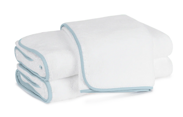 A neatly folded stack of white towels with light blue trim from the Matouk Giza Bath Collection, Hydrangea, made using Giza extra long-staple cotton for exceptional softness and durability.