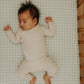 A baby in a striped onesie sleeps, arms raised, on the Gooselings Green Picnic Gingham Crib Sheet, made with OEKO-TEX certified cotton sateen in light green and white checks.