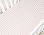 A close-up of a Gooselings Picnic Gingham Pink Crib Sheet, made from extra soft cotton sateen in pink and white, covering a crib mattress inside a white crib.