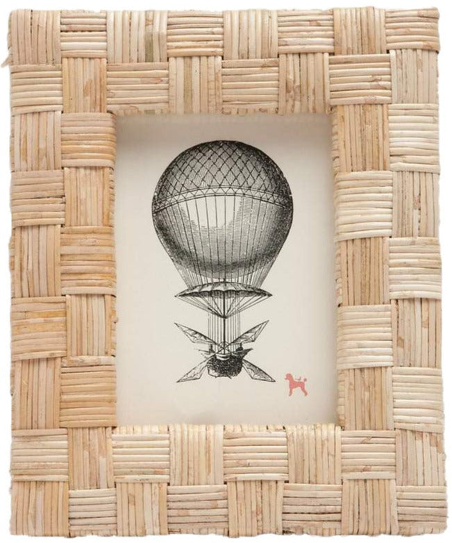 The Grasse Frame Collection by Pigeon & Poodle features a rattan woven frame with an extra-thick profile, displaying a vintage hot air balloon illustration and a small red dog icon in the lower right corner.