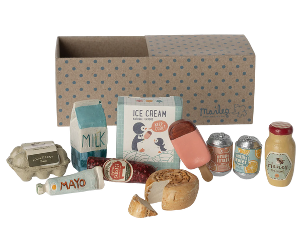 The Maileg Miniature Grocery Box by Maileg includes a delightful assortment of toy groceries, such as a milk carton, ice cream, cans of fizzy drinks, a jar of honey and jam, eggs, a bread loaf, a mayo tube, and comes with a cardboard box for storage – perfect for engaging in pretend play.