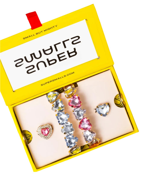 A yellow gift box labeled "Super Smalls" contains the Super Smalls Heart to Heart Mega Set, featuring colorful jeweled accessories such as a bracelet with heart-shaped gems and two adjustable rings.