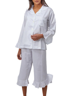 A person wears Haute Home's Ruffle Pajamas, a white cotton sateen set with long sleeves, cropped bottoms, and ruffle trim, standing against a white background.