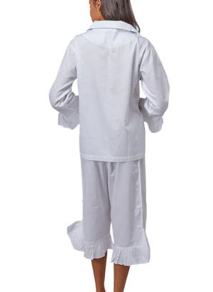 A person is shown from the back, wearing Haute Home’s Ruffle Pajamas—a white cotton sateen set with ruffle trim on the cuffs and hems—against a plain white background.