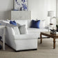 A modern living room with white furniture, blue accent pillows, a Hickory Chair Ceylon Cocktail Table, a decorative cabinet, and a table lamp beside a window with sheer curtains brings the sophisticated charm of West Palm Beach into your home.