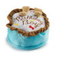 The Haute Diggity Dog Birthday Boy Toy is a round, squeaky dog birthday cake toy with blue sides, brown trim, "Birthday Boy" embroidery, felt bones, and two bone-shaped accents.