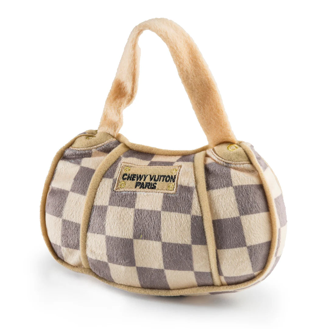 The Haute Diggity Dog Checker Chewy Vuiton Handbag is a plush, squeaky dog toy designed to resemble a designer handbag with a checkered pattern and a "Chewy Vuiton Paris" label.