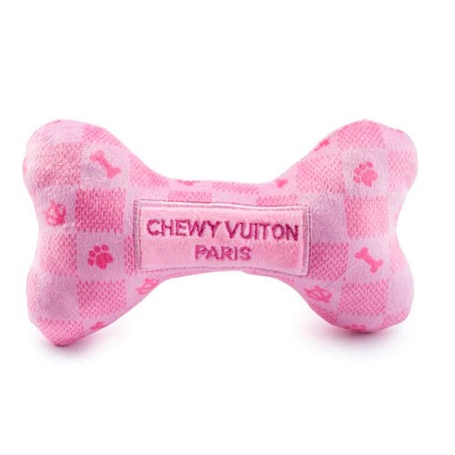 The Pink Checker Chewy Vuiton Bone by Haute Diggity Dog is a plush, squeaky pink bone dog toy with a checkered pattern, playful icons, and "CHEWY VUITON PARIS" embroidered at the center.