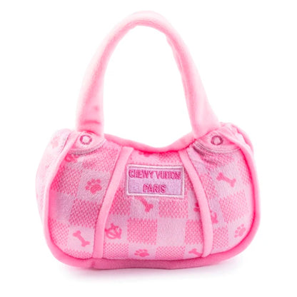 The Pink Chewy Vuiton Handbag by Haute Diggity Dog is a small, pink plush dog toy with checkered pattern, paw prints, and bones. The front label reads "CHEWY VUITON PARIS.