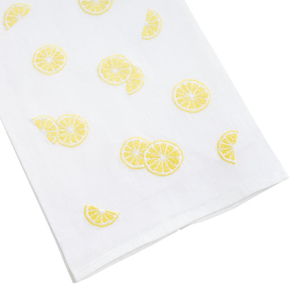 White 100% linen Lemon Slice Tip Towel with a pattern of yellow lemon slices, spread out on a plain background by Haute Home.