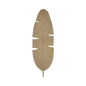 The Johanna Ortiz Mythic Ecosystem Table Mat Collection features a jute mat shaped like a banana leaf with notched edges, reminiscent of leaf-shaped placemats, shown on a white background.