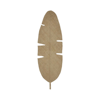 The Johanna Ortiz Mythic Ecosystem Table Mat Collection features a jute mat shaped like a banana leaf with notched edges, reminiscent of leaf-shaped placemats, shown on a white background.