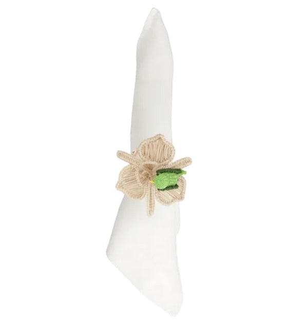 A white cloth napkin is folded and held by the Mercedes Salazar Pajarito Napkin Ring, handmade in Colombia from raffia fiber, featuring a beige floral design with a small green accent in the center.