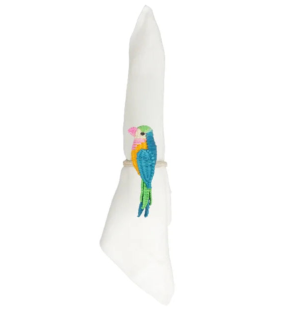 Each of the two white cloth napkins is wrapped with a Mercedes Salazar Parakeet Napkin Ring, handmade and featuring a vibrant embroidered parrot design.