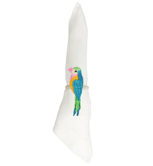 Each of the two white cloth napkins is wrapped with a Mercedes Salazar Parakeet Napkin Ring, handmade and featuring a vibrant embroidered parrot design.
