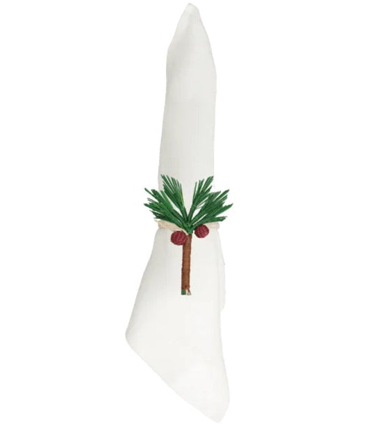A white cloth napkin folded upright with an embroidered green palm tree and two coconuts on the front, elegantly accented by the Mercedes Salazar Coconut Palm Tree Napkin Ring, handmade in Colombia.