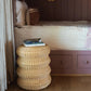 The Maggie Side Table by Varnish Collection, topped with books, sits beside a bed with white bedding and a brown accent pillow in a wood-paneled room, bringing a vintage touch to the space.