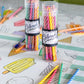 Two reusable clear tubes containing sets of vibrant Hester & Cook Colored Pencils, resting on a sheet of paper featuring hand-drawn ice cream illustrations.