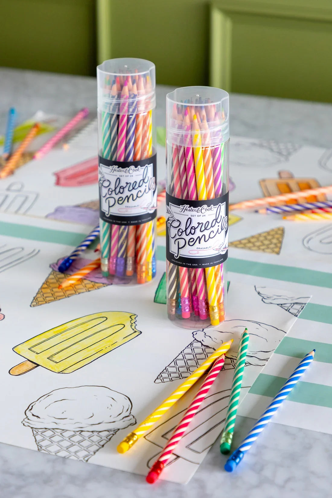 Two reusable clear tubes containing sets of vibrant Hester & Cook Colored Pencils, resting on a sheet of paper featuring hand-drawn ice cream illustrations.