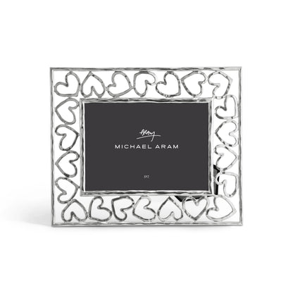 A silver photo frame from the Heart Frame Collection by Michael Aram features a heart-patterned border and a branded placeholder card, celebrating handcraftsmanship and love in every detail.