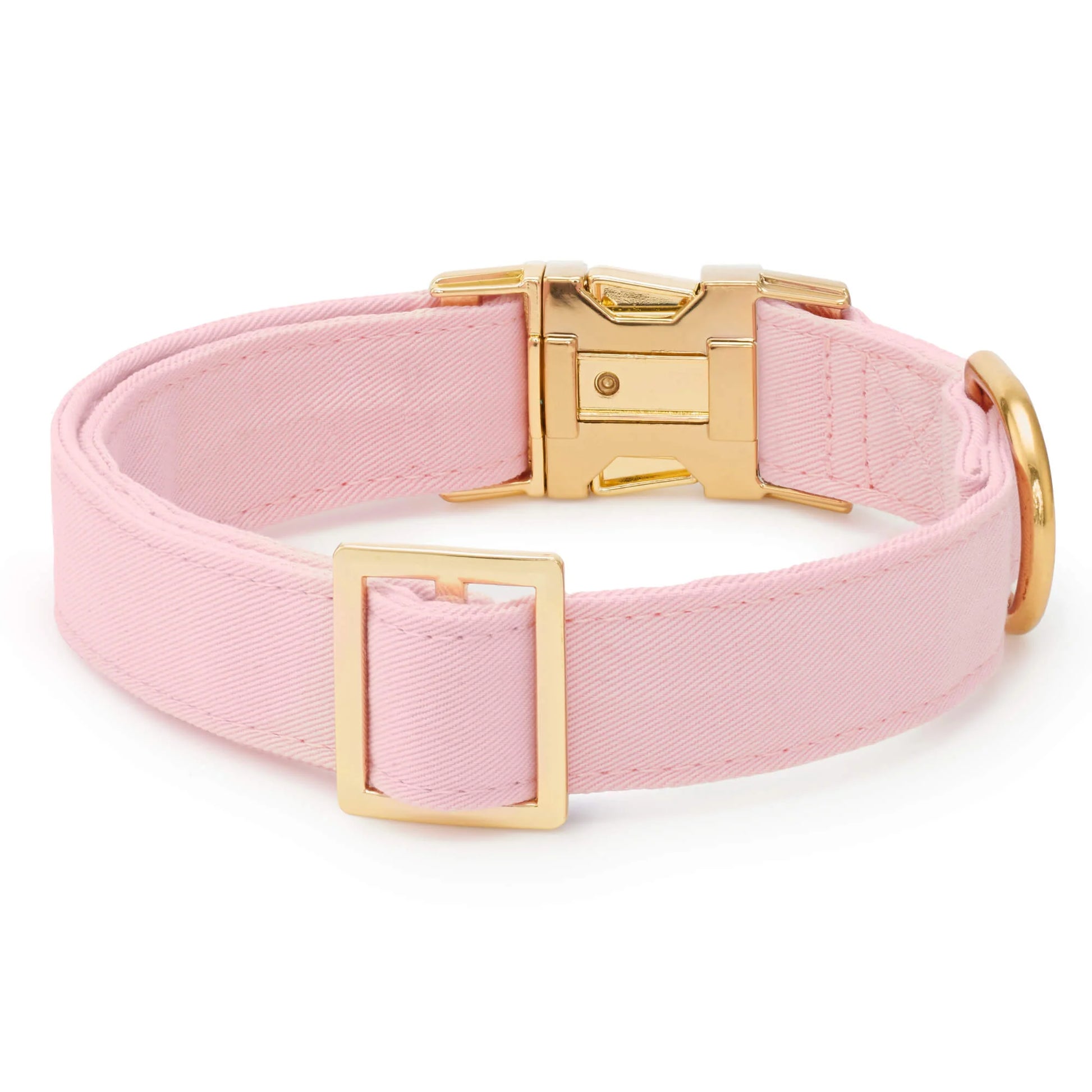 The Blush Pink Dog Collar by The Foggy Dog is crafted from light pink fabric and features a gold metal buckle, D-ring, and adjustment slider. This elegant pet accessory is showcased on a plain white background.