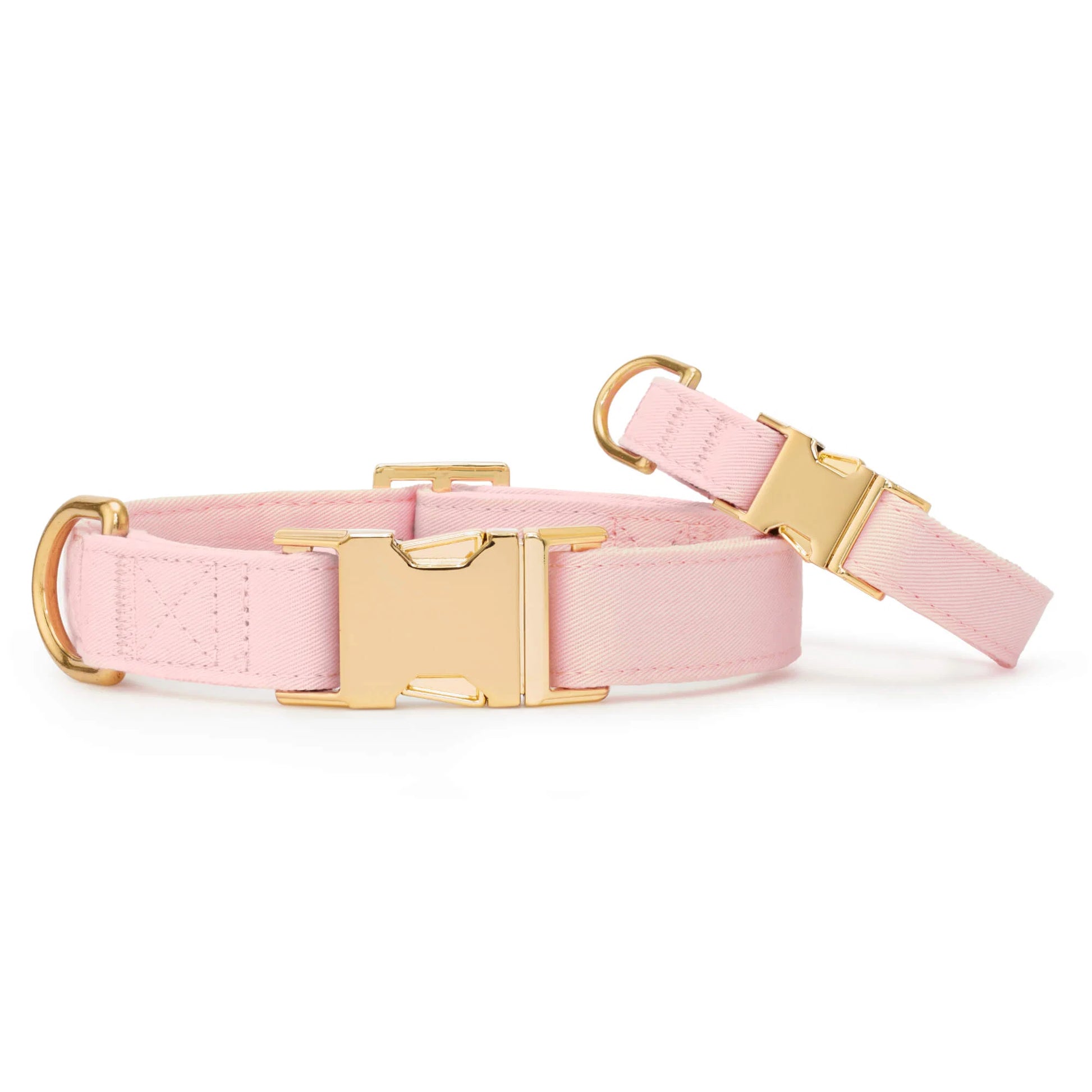 Two Blush Pink Dog Collars by The Foggy Dog, crafted from soft fabric and adorned with gold metal buckles and D-rings, are displayed against a white background—a stylish accessory for your furry friend.