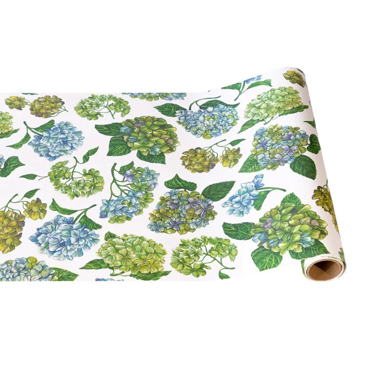 The Paper Runner Collection by Hester & Cook features wrapping paper with blue, yellow, and green hydrangea flowers on white—ideal for standout gift wrap or as a creative table runner in your dining area.