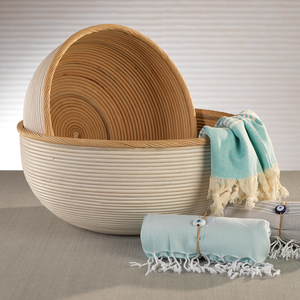 The Santo Rattan Bowl Collection by Zodax features two artisanal bowls with light wood and white finishes, displayed beside blue and white fringed cloths on a neutral surface.