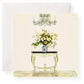 A floral arrangement in a patterned vase sits on a small ornate table beneath a chandelier, with Karen Adams Dolce Vita Gift Enclosures and a white envelope in the background.