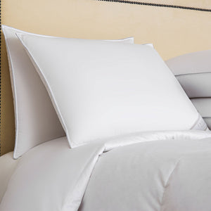 A neatly made bed features two Frette Cortina Firm Density Pillow Inserts and a white comforter, all wrapped in luxurious cotton sateen, set against a beige headboard.