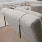 Close-up of a textured Sway Lounge Chair beige chair with a rope and brass weight draped over the back. Modern white furniture from Pure by Hive and a glass table are in the background on a wooden floor, evoking the breezy elegance of West Palm Beach.
