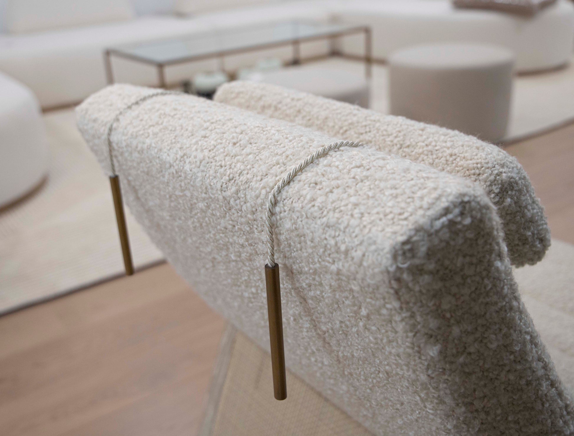 Close-up of a textured Sway Lounge Chair beige chair with a rope and brass weight draped over the back. Modern white furniture from Pure by Hive and a glass table are in the background on a wooden floor, evoking the breezy elegance of West Palm Beach.