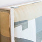 Edge of a rectangular abstract art canvas painting in neutral tones, mounted in a light-colored wooden frame that complements the wood details of the Highland House Gustav Bed, King upholstered headboard.