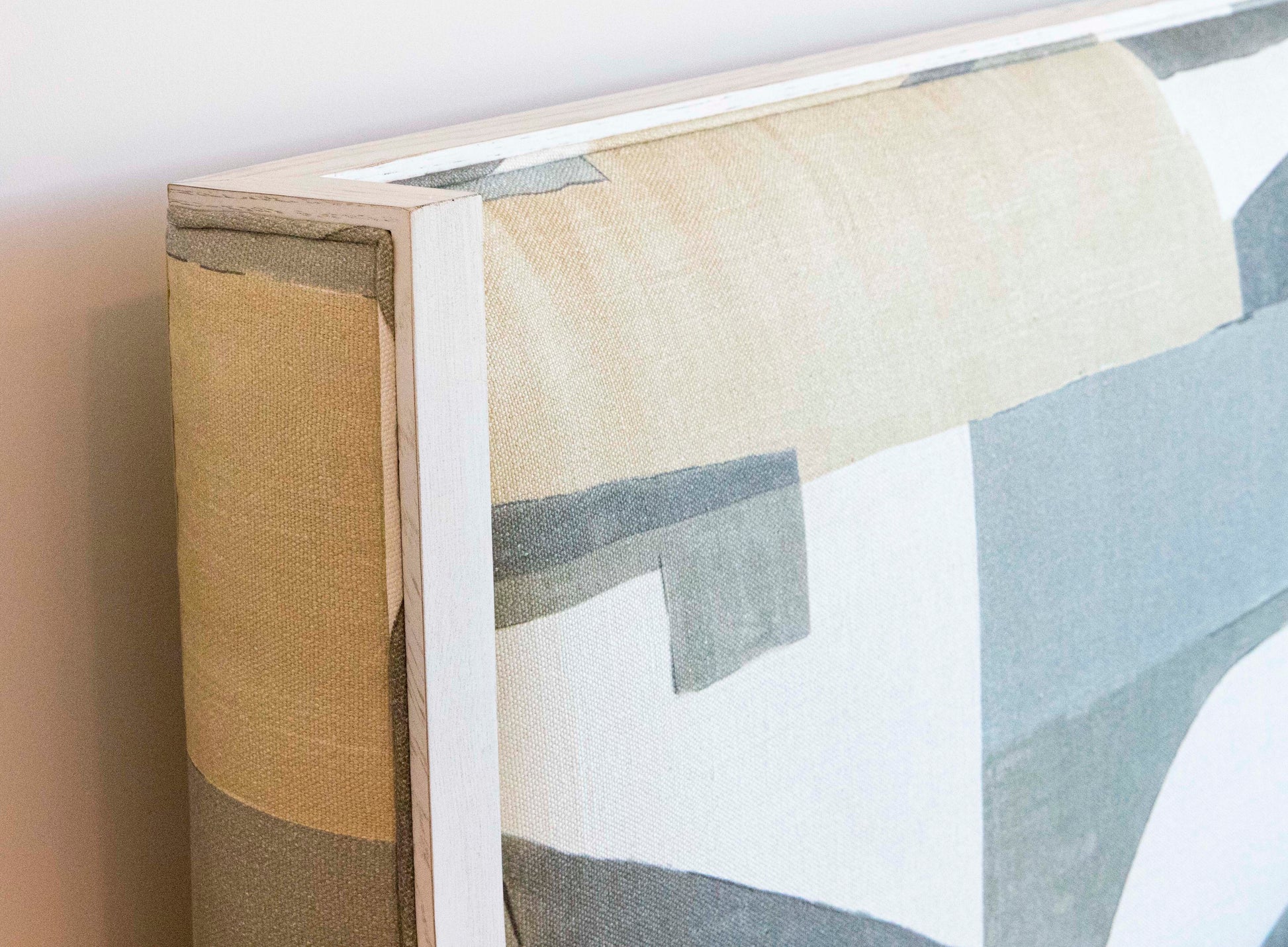Edge of a rectangular abstract art canvas painting in neutral tones, mounted in a light-colored wooden frame that complements the wood details of the Highland House Gustav Bed, King upholstered headboard.